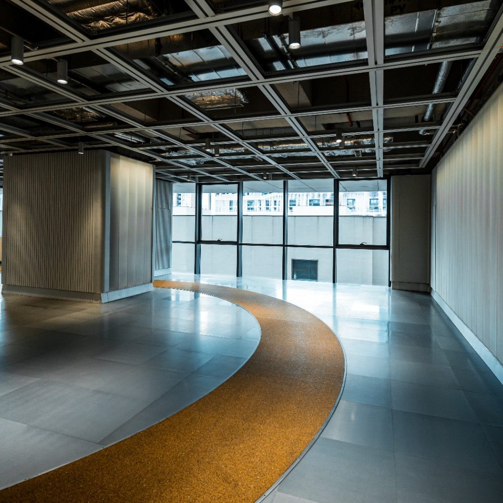 Professional commercial interior painting in Jacksonville Beach, featuring a modern open office floor plan with polished gray tile flooring, an inlaid curved yellow accent stripe, expansive glass windows, and an exposed industrial ceiling grid.