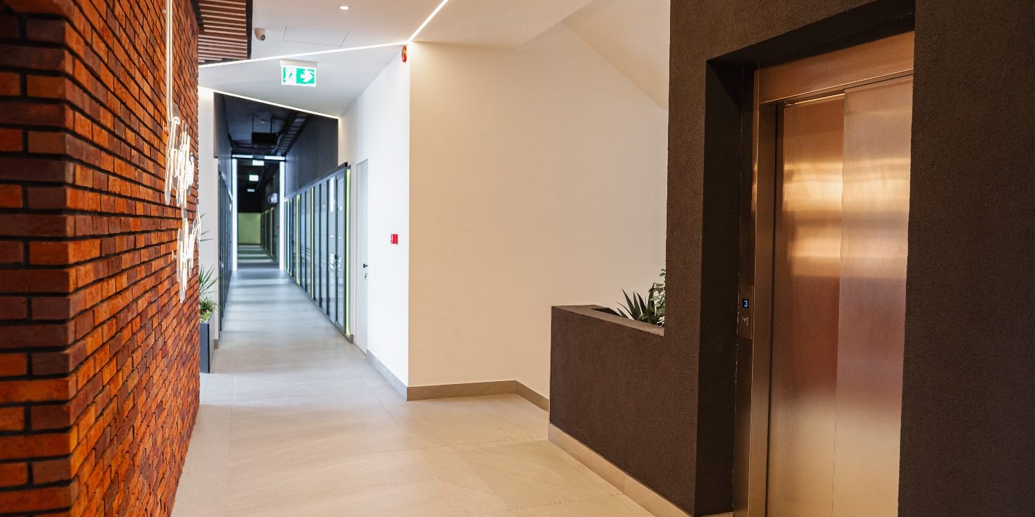Professional commercial interior painting in Jacksonville Beach, featuring a modern office hallway with a polished tile floor, exposed brick accent walls, a sleek metallic elevator door, and clean lighting under a bright ceiling.