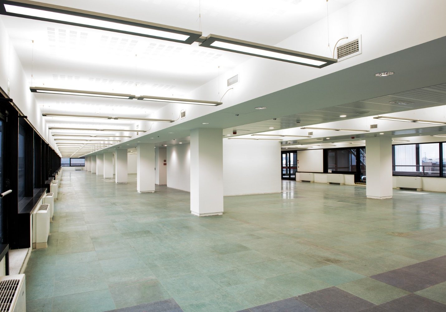Professional commercial interior painting in Jacksonville Beach, featuring a modern open office floor plan with polished gray tile flooring, an inlaid curved yellow accent stripe, expansive glass windows, and an exposed industrial ceiling grid.